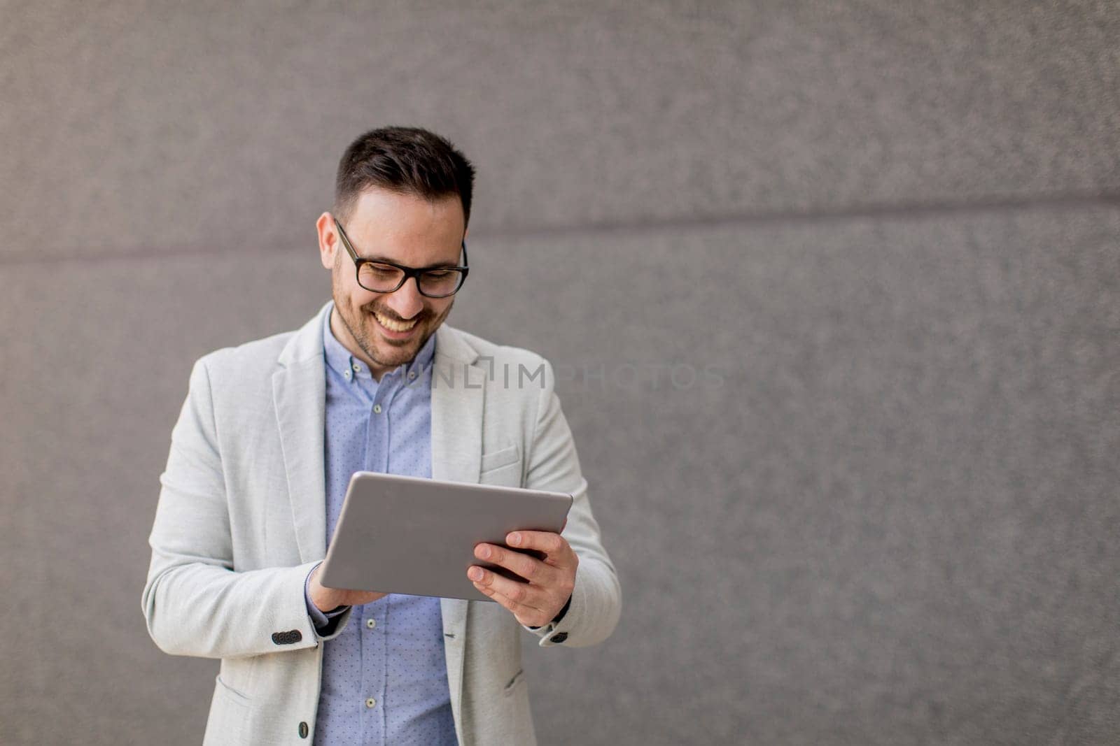 Handsome young businessman with digital tablet by the grey wall