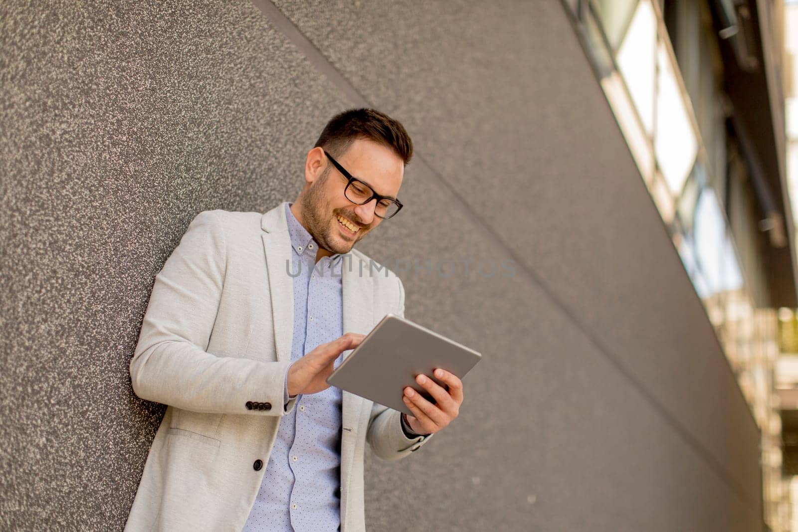 Handsome young businessman with digital tablet by the grey wall