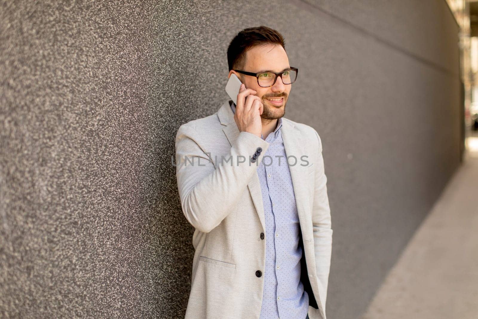 Handsome young businessman with mobile phone by the grey wall