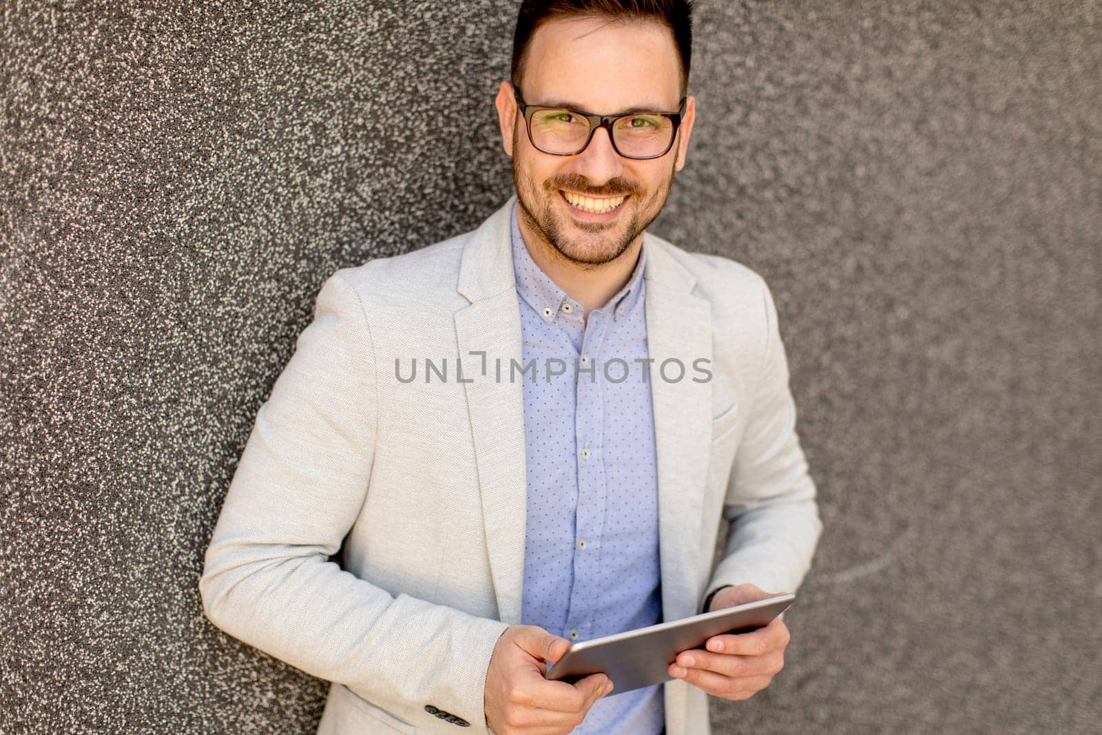 Handsome young businessman with digital tablet by the grey wall