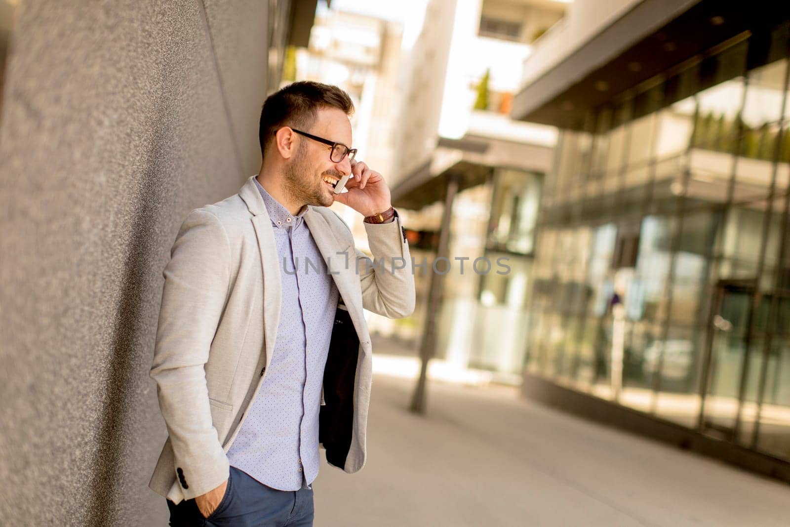 Handsome young businessman with mobile phone by the grey wall