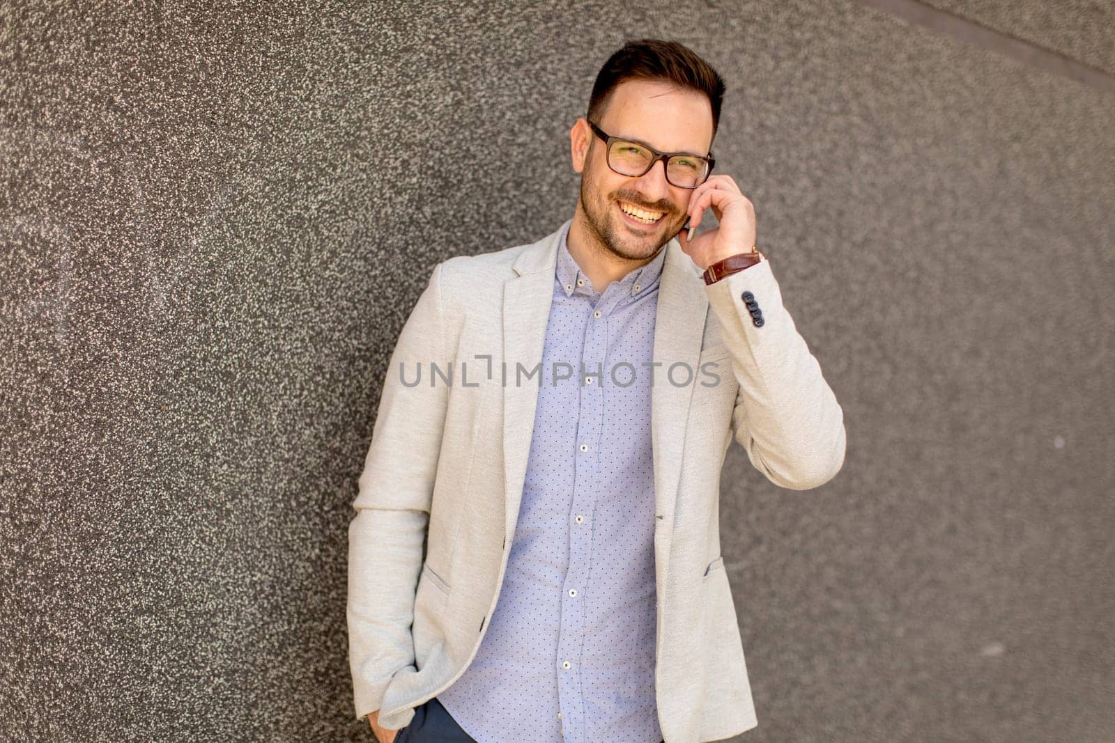 Handsome young businessman with mobile phone by the grey wall