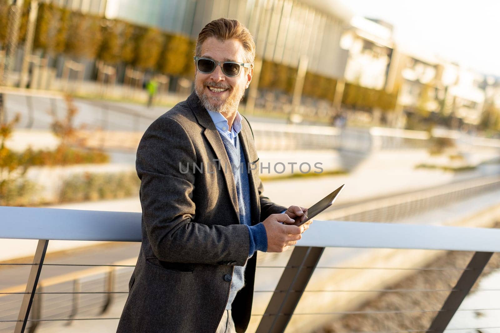 A stylish man stands on a balcony, engaging with a tablet against a backdrop of sleek architecture.