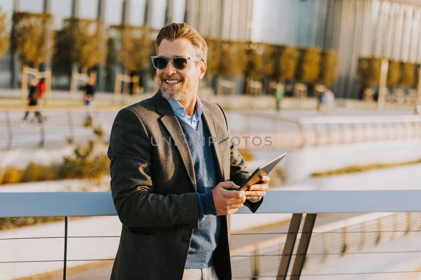 A stylish man stands on a balcony, engaging with a tablet against a backdrop of sleek architecture.