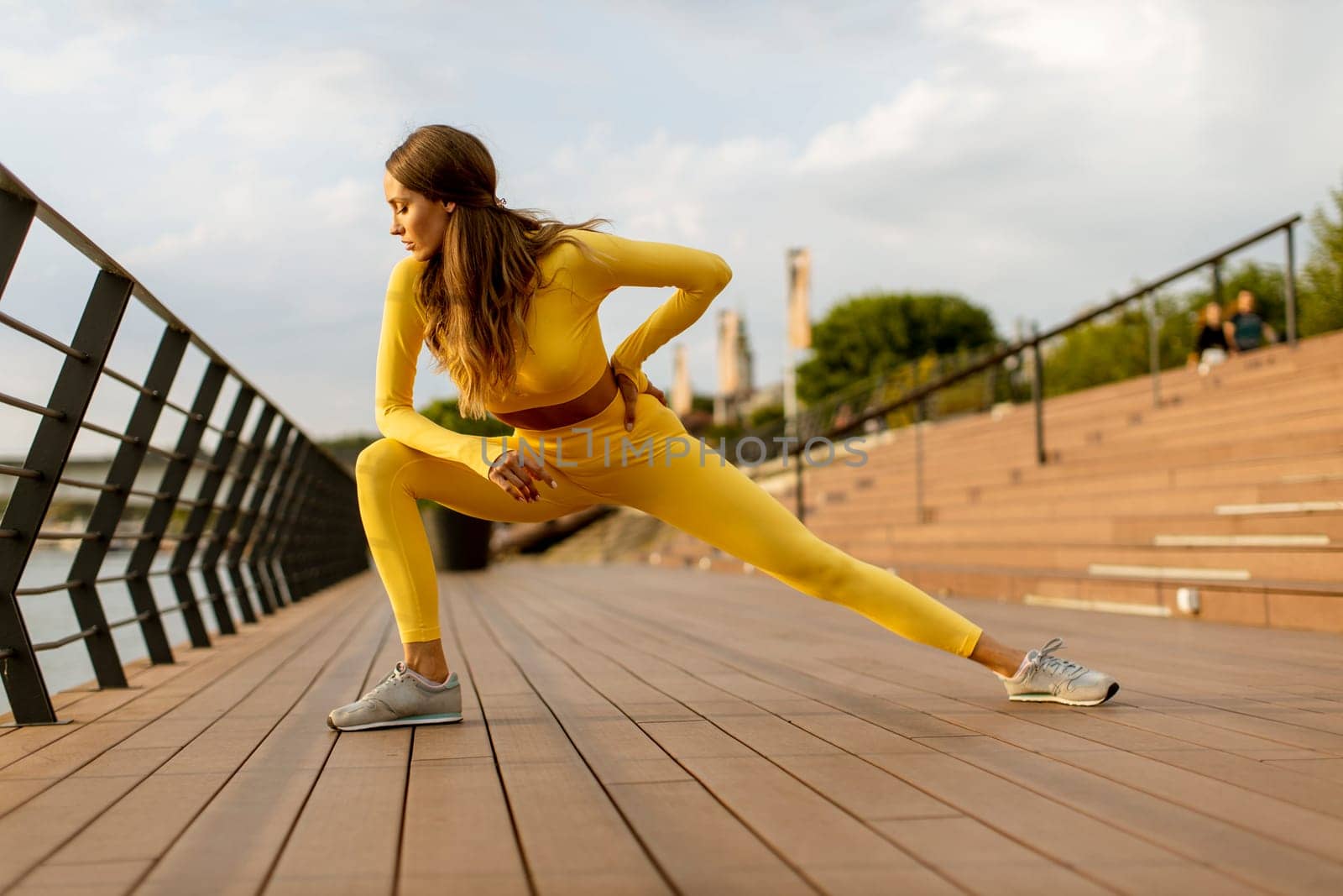 Pretty young woman having stretching exercise on the riverside pier
