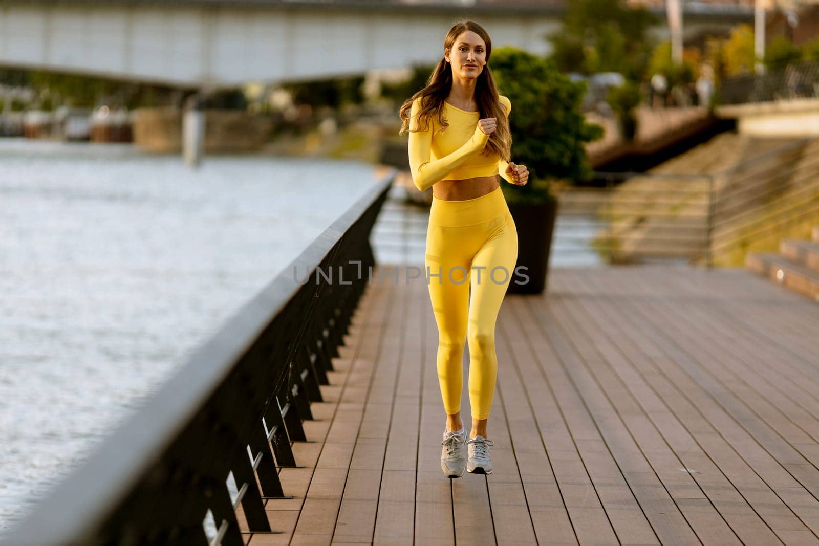 Pretty young woman running exercise on the riverside pier