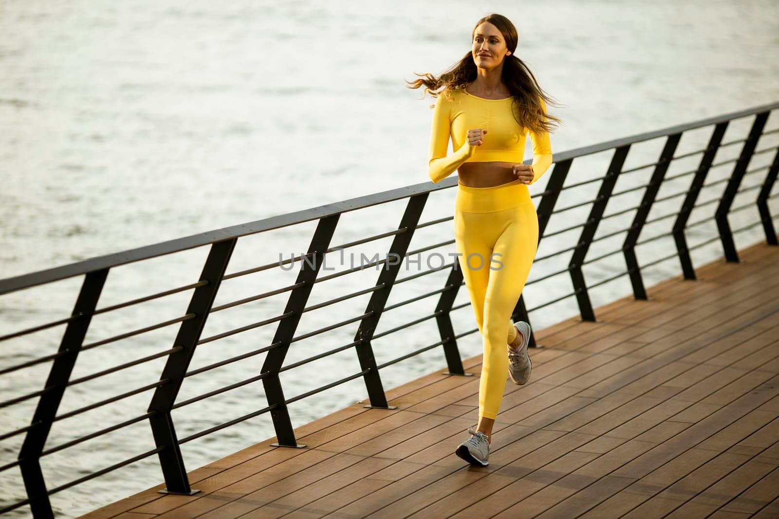 Pretty young woman taking running exercise by the river promenade