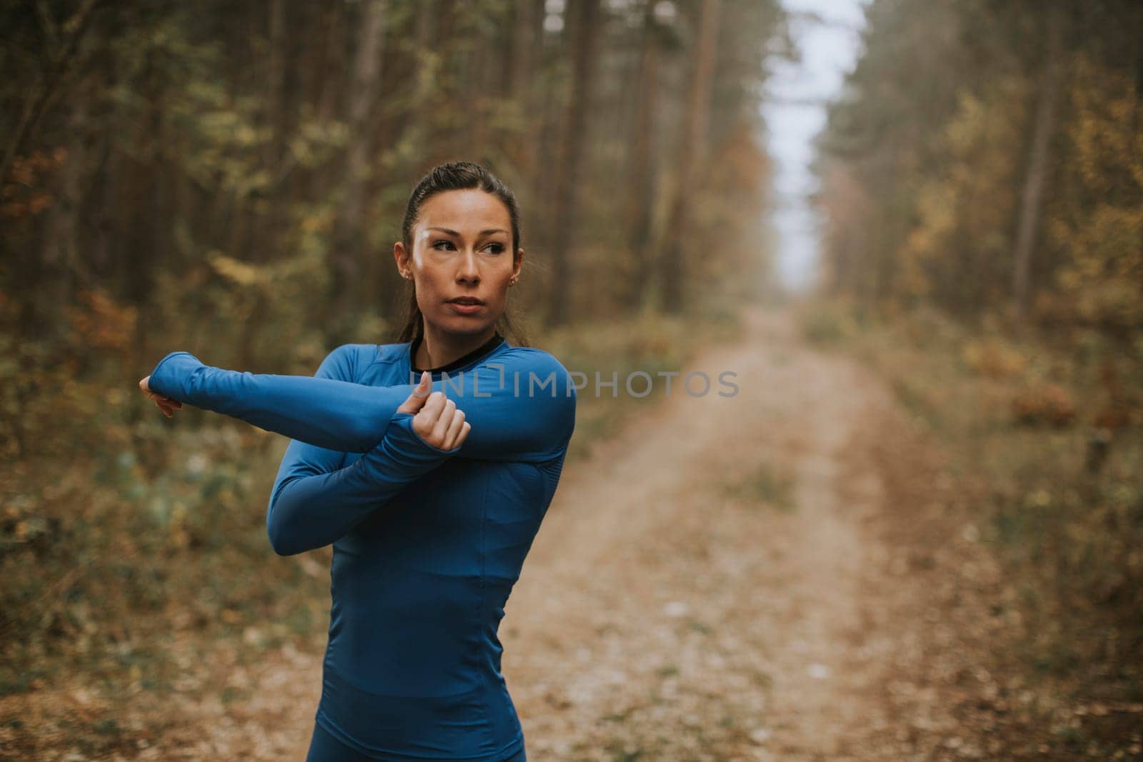 Pretty young woman in blue track suit stretching before workout in the autumn forest