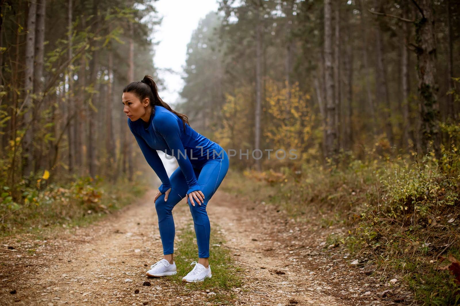 Pretty young woman take a break during outdoor exercise on the forest trail at autumn