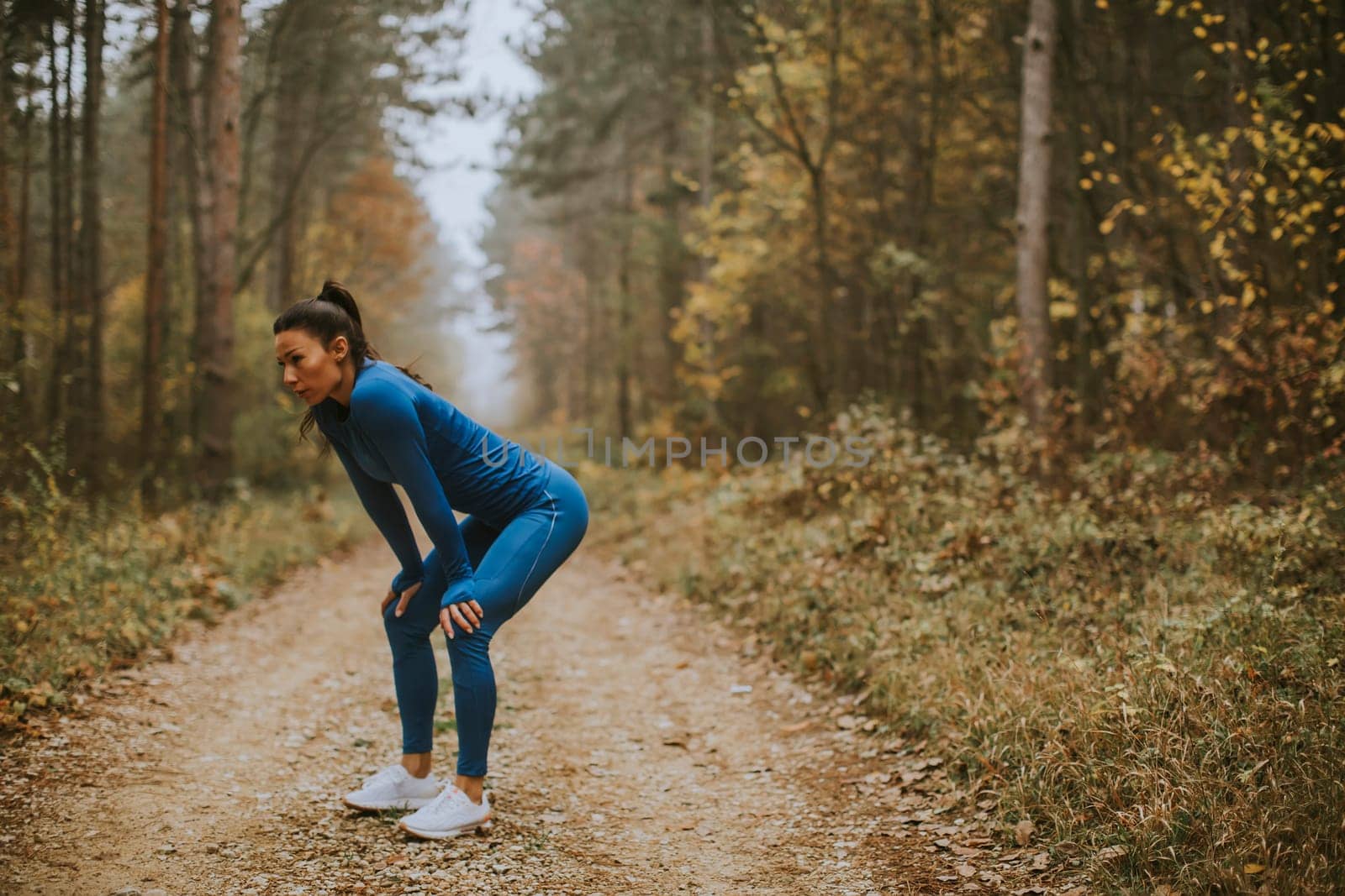 Pretty young woman take a break during outdoor exercise on the forest trail at autumn