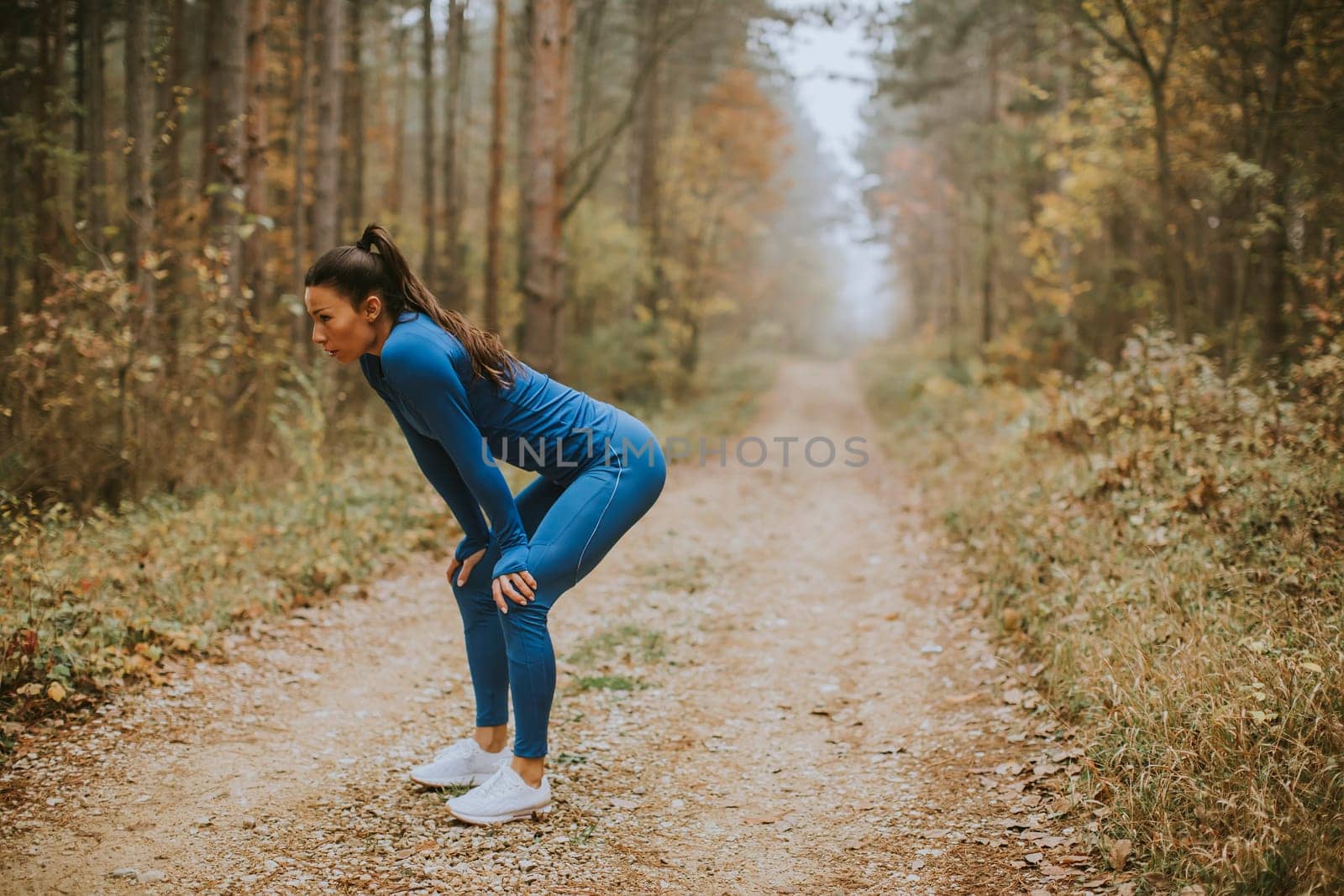 Pretty young woman take a break during outdoor exercise on the forest trail at autumn