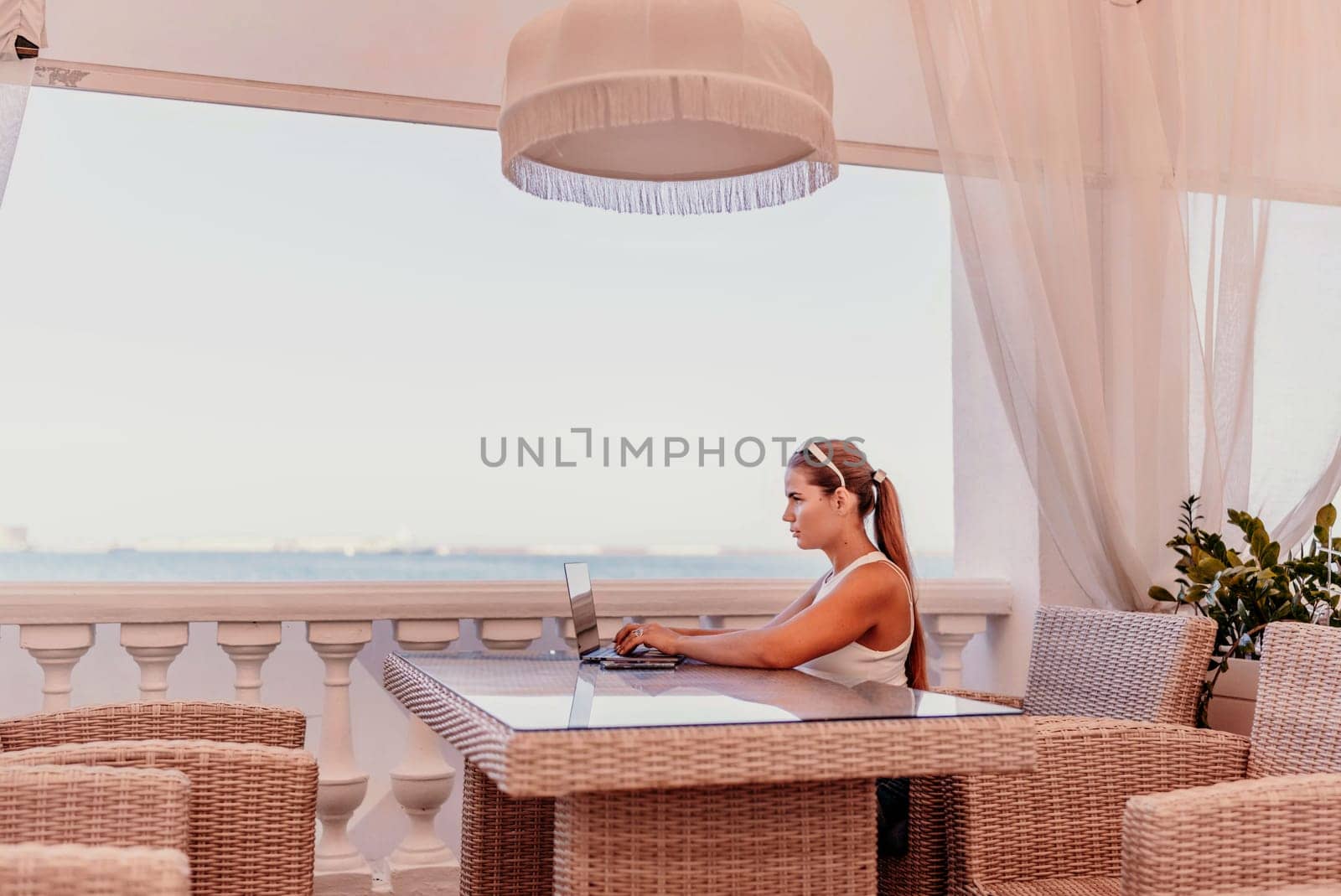 Woman coffee cafe laptop sea. Female freelancer using laptop on coffee break in modern cafe with sea view in the morning.