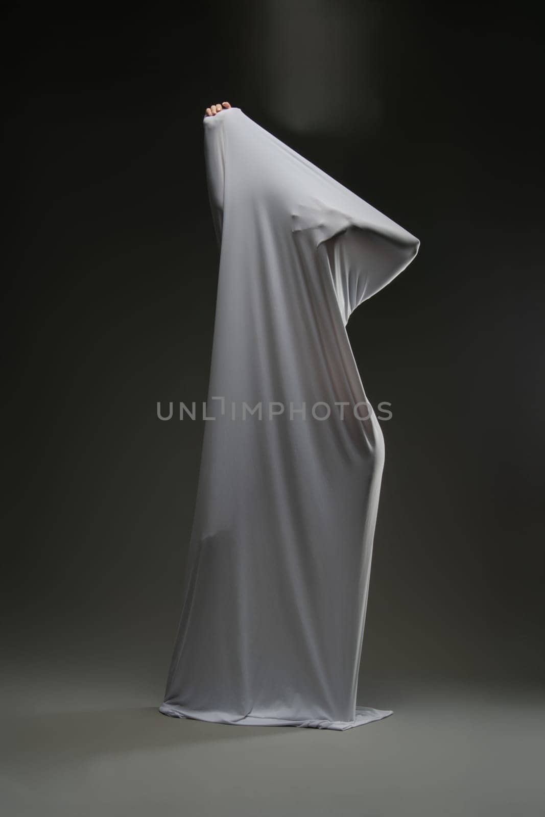 A woman playfully showcases her beauty while draped in soft, sheer fabric against a dark background.