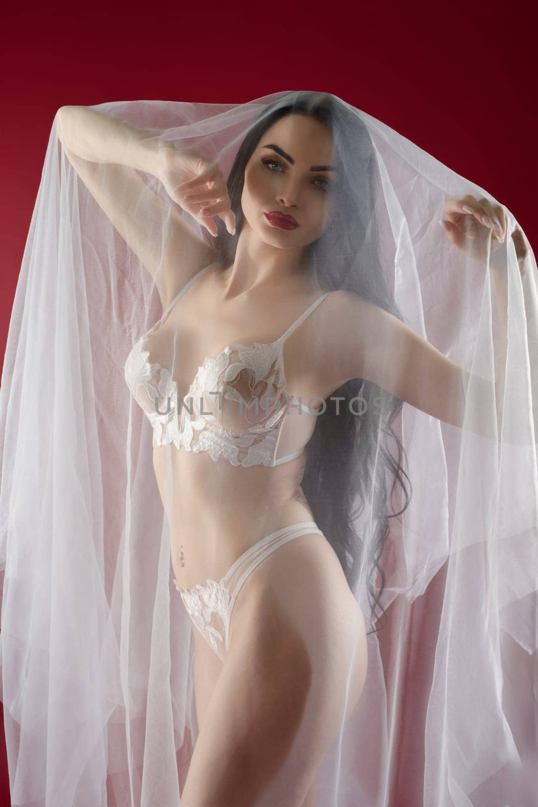 A beautiful woman poses gracefully in lingerie, draped in soft fabric, creating an enchanting bridal atmosphere.