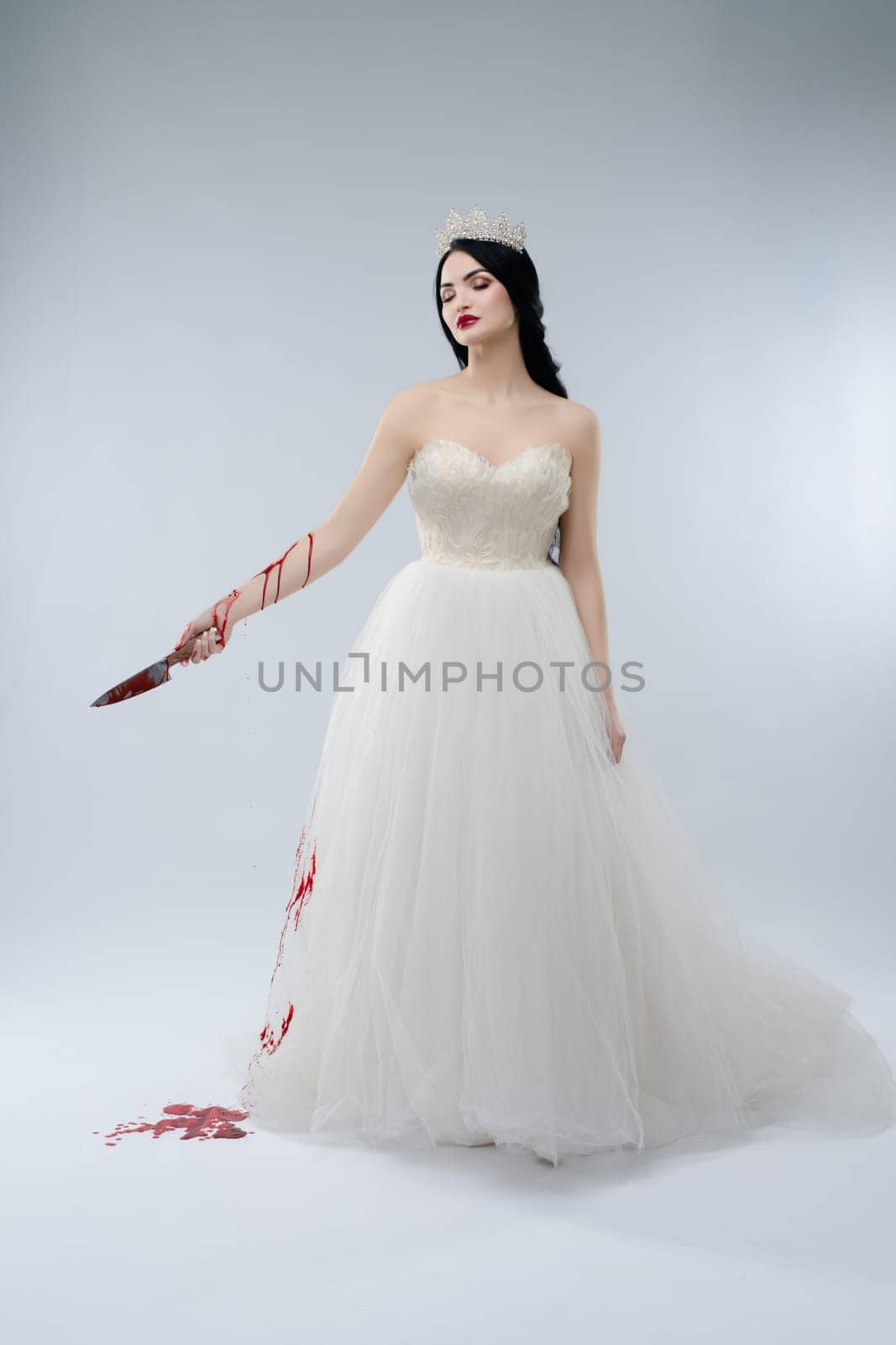 A woman dressed as a bride stands confidently, holding a knife with blood dripping, challenging traditional beauty.