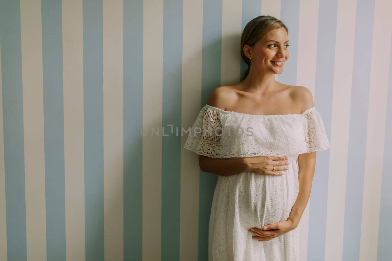Pretty young pregnant woman standing by the wall in the room