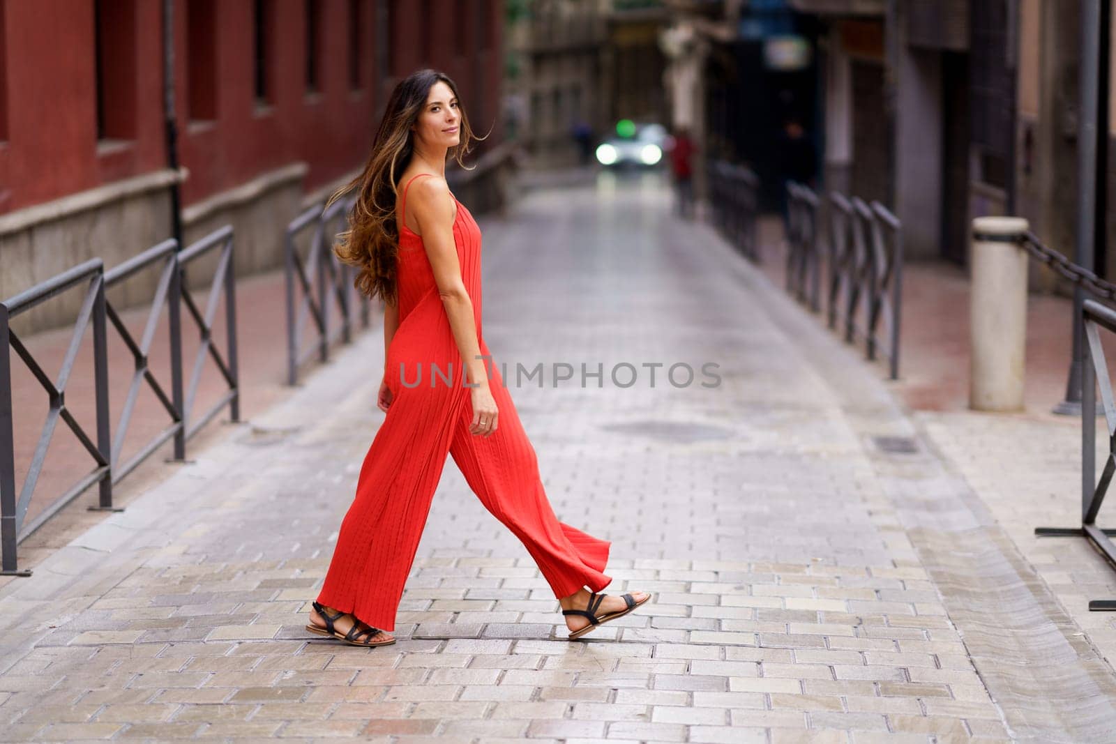 In a vibrant city, a fashionable woman confidently walks down a tranquil street in a striking red jumpsuit, showcasing her unique style and elegance, captivating everyone with her grace and poise