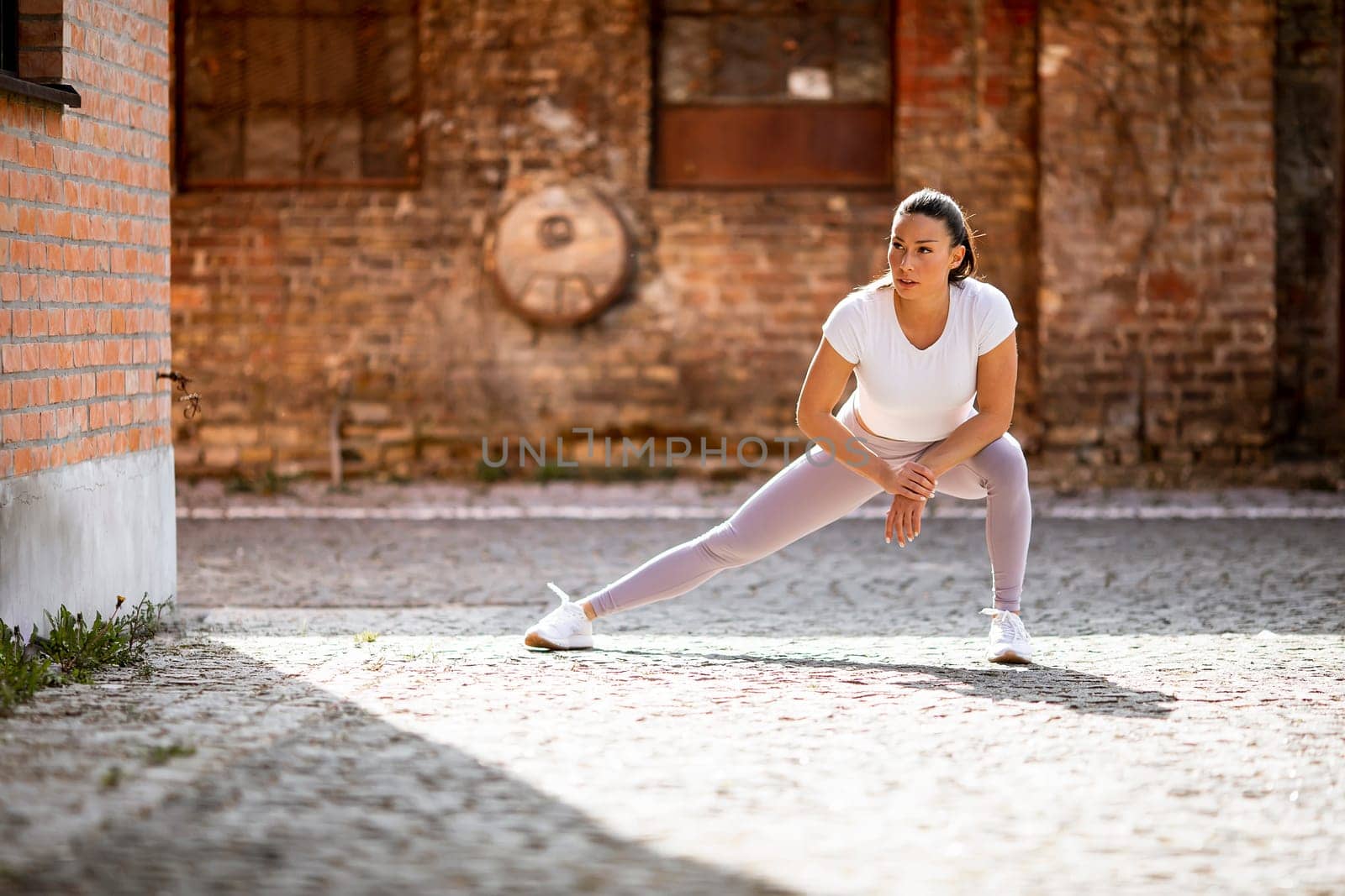 Pretty young woman stretching during training in the urban environment