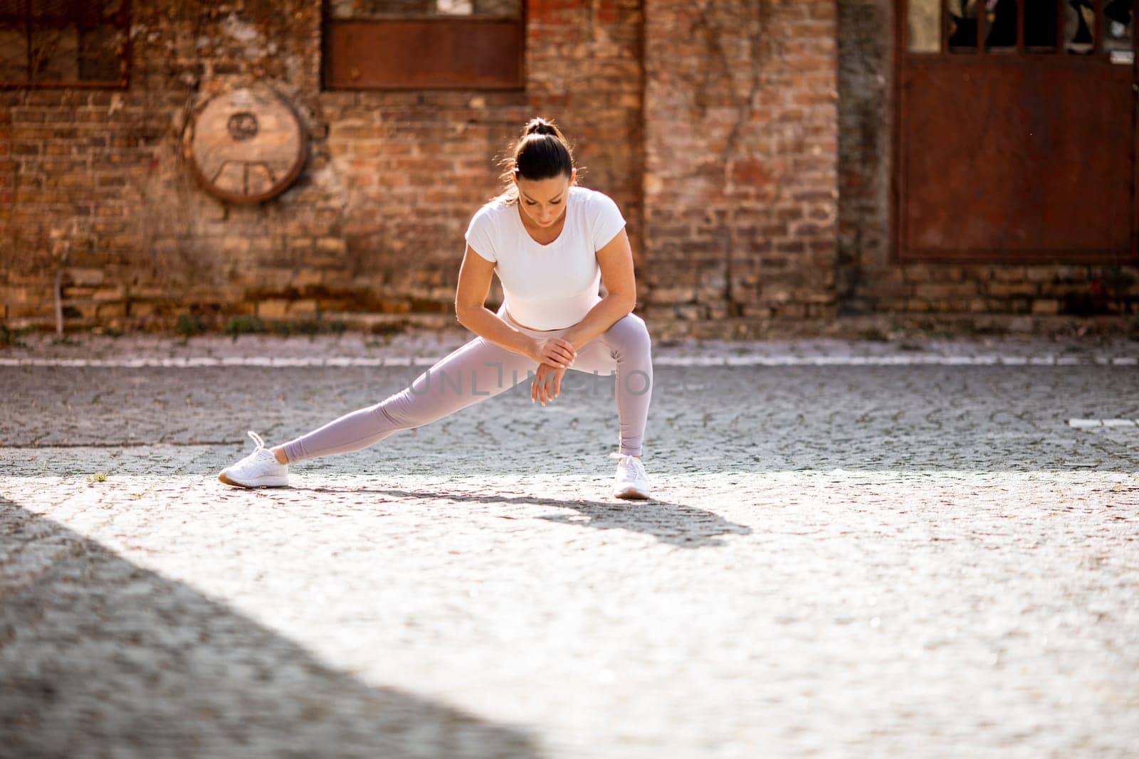 Pretty young woman stretching during training in the urban environment