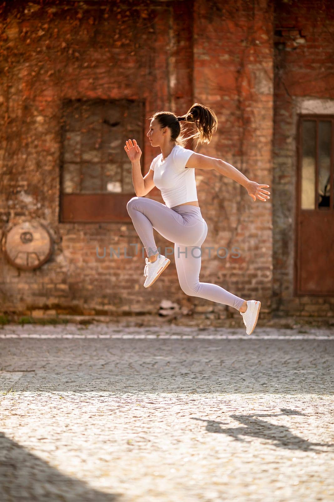 Pretty young woman juping high during training in the urban environment
