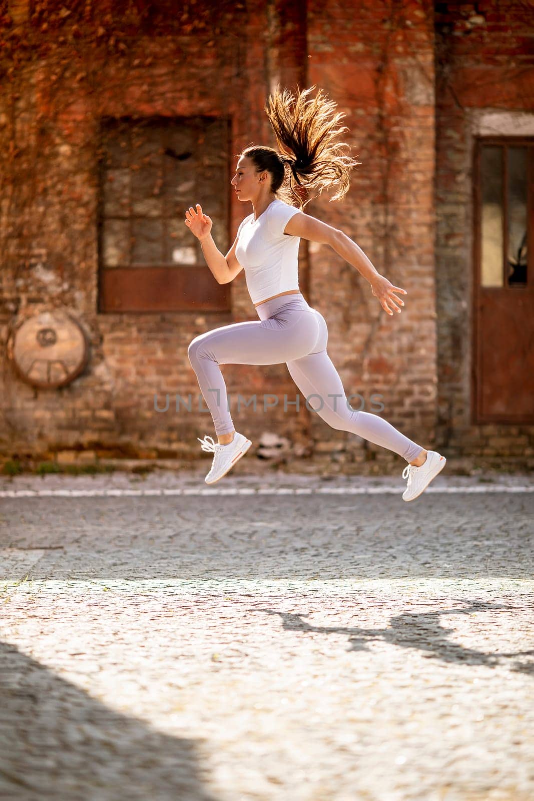 Pretty young woman juping high during training in the urban environment