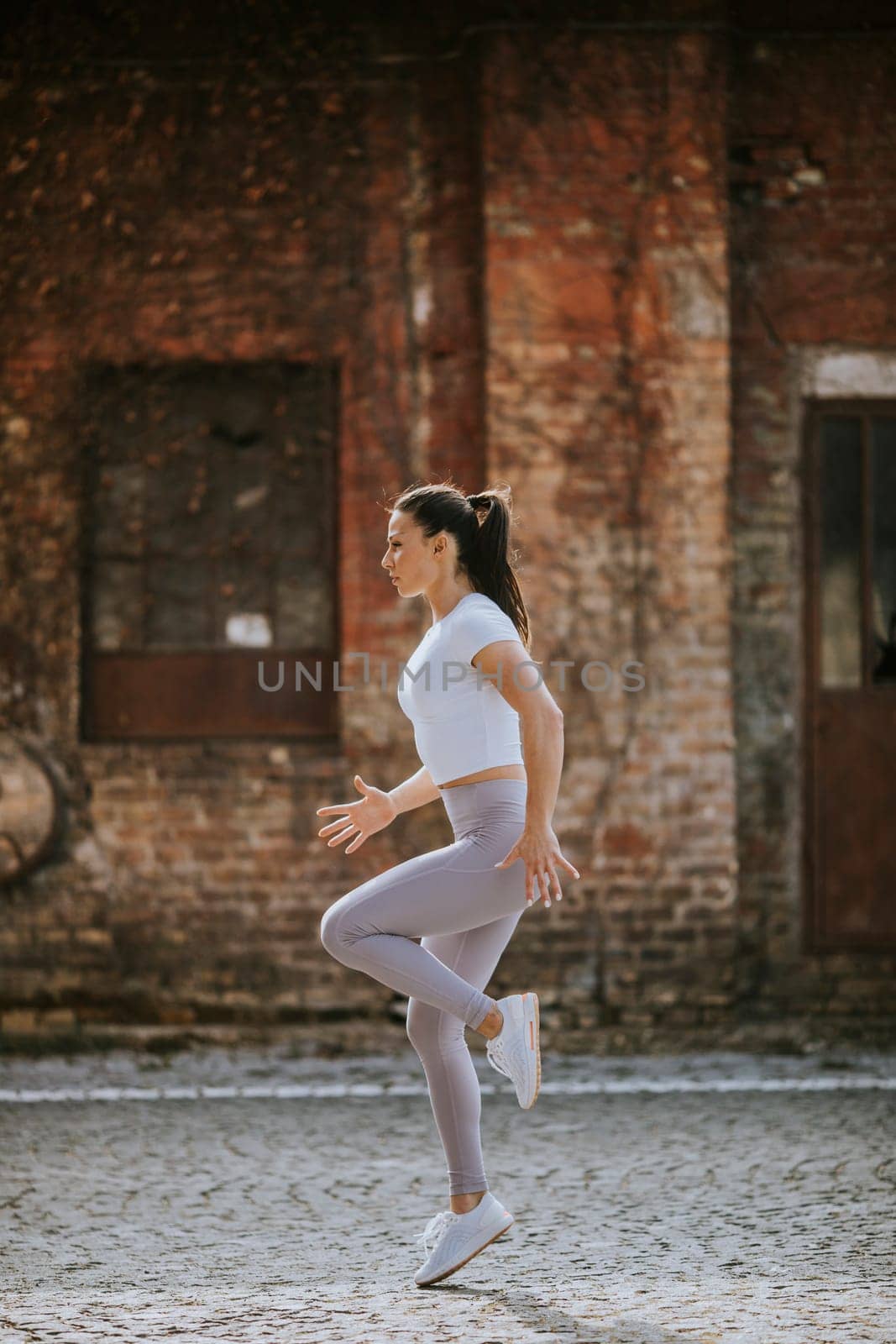 Pretty young woman warming before running in the urban environment