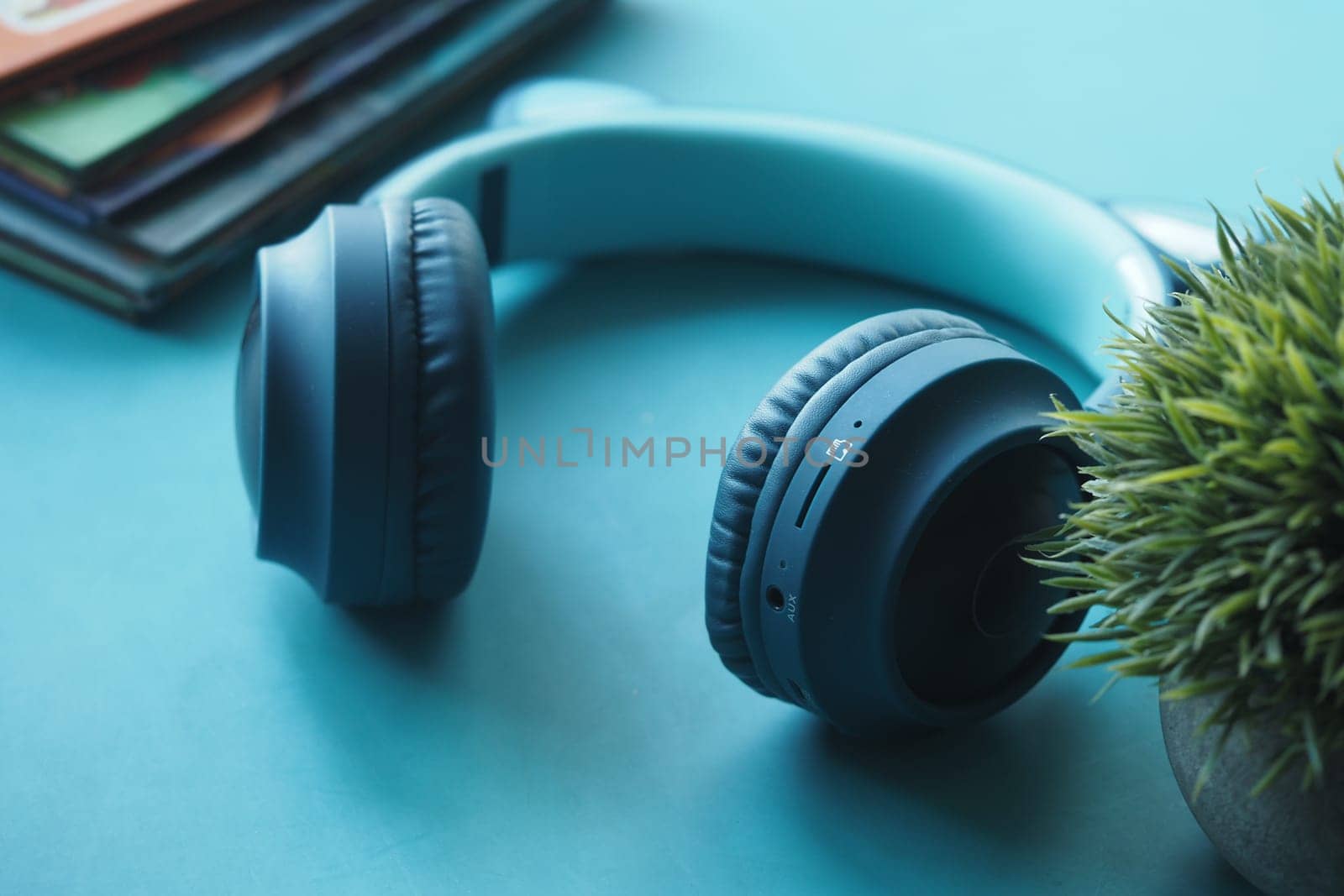 Bright teal surface features headphones, a small plant, and stacked books.