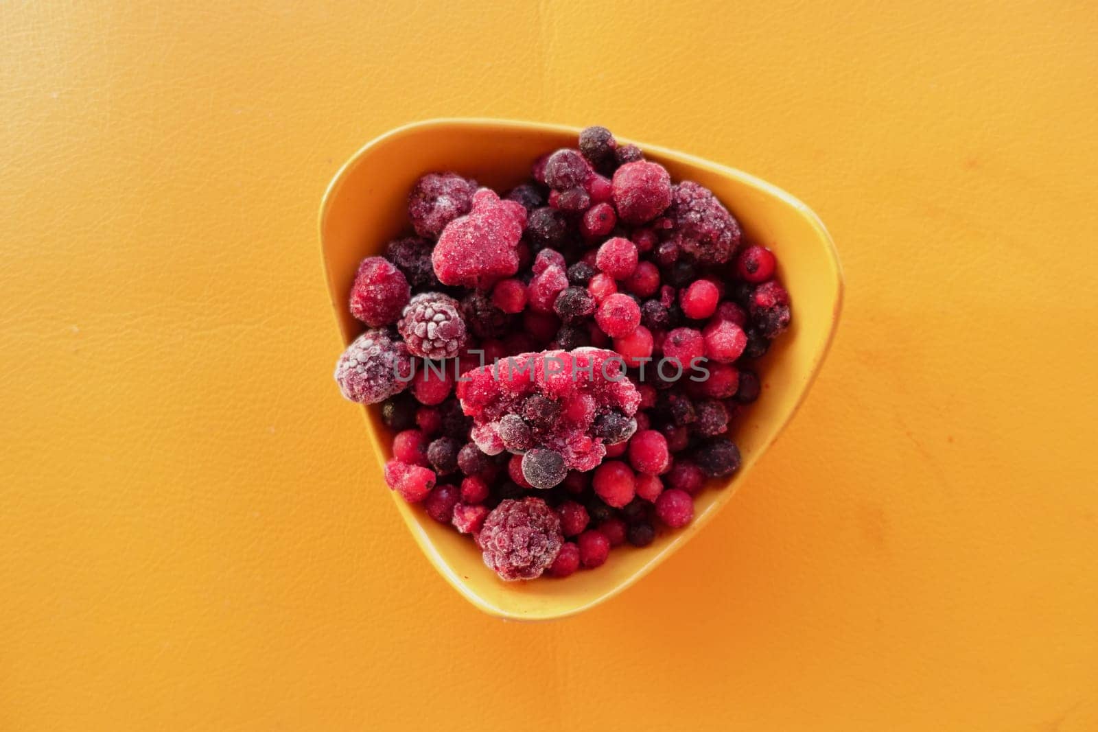 A bowl filled with assorted frozen berries sits on a bright surface.