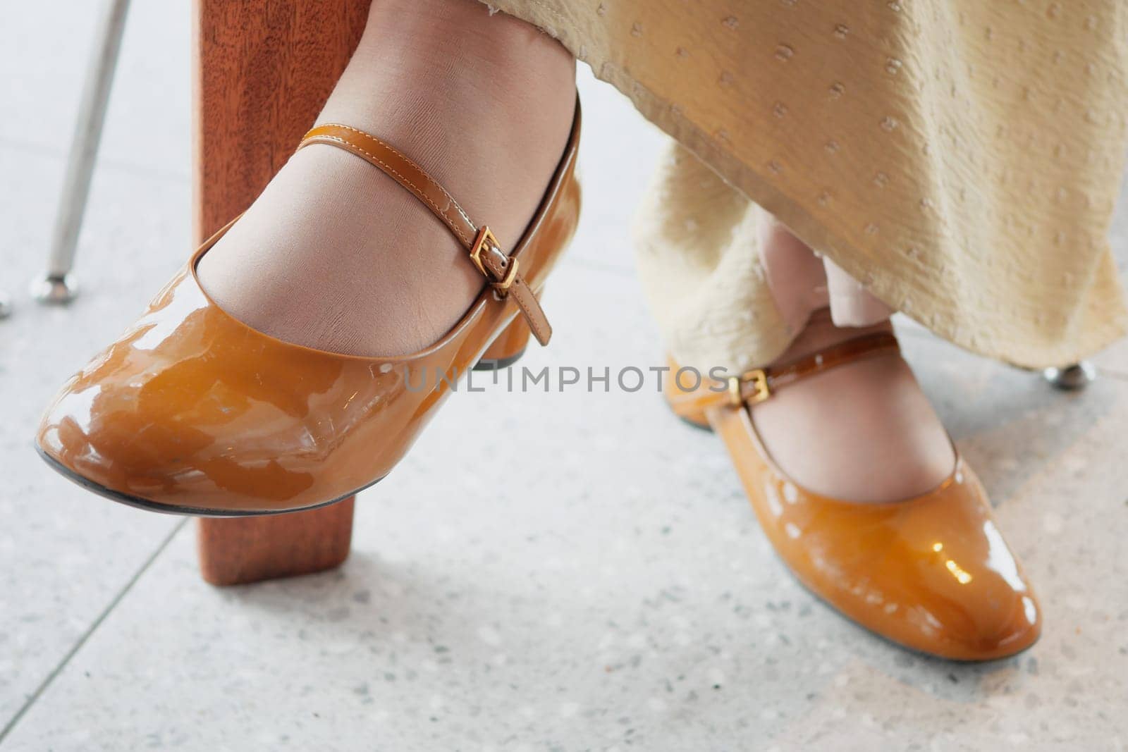 Brown patent leather shoes enhance a woman's elegant dress in a cafe.