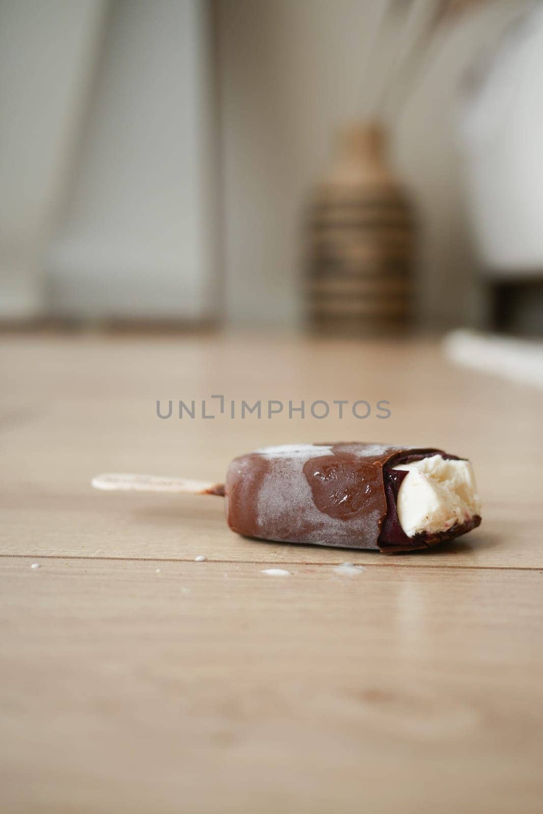 A chocolate-coated popsicle lies on a wooden floor, partially melted.
