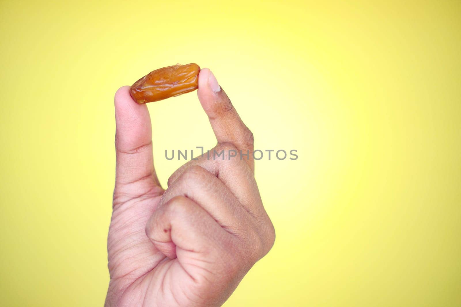 A hand displays a single date fruit showcasing its rich texture.