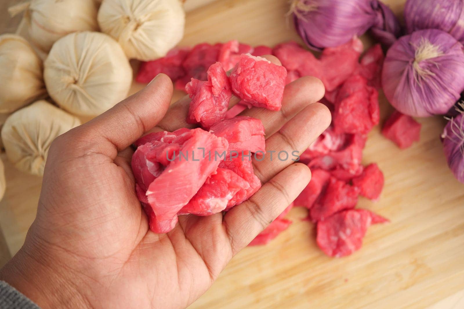 A hand holds raw beef pieces surrounded by spices and onions.