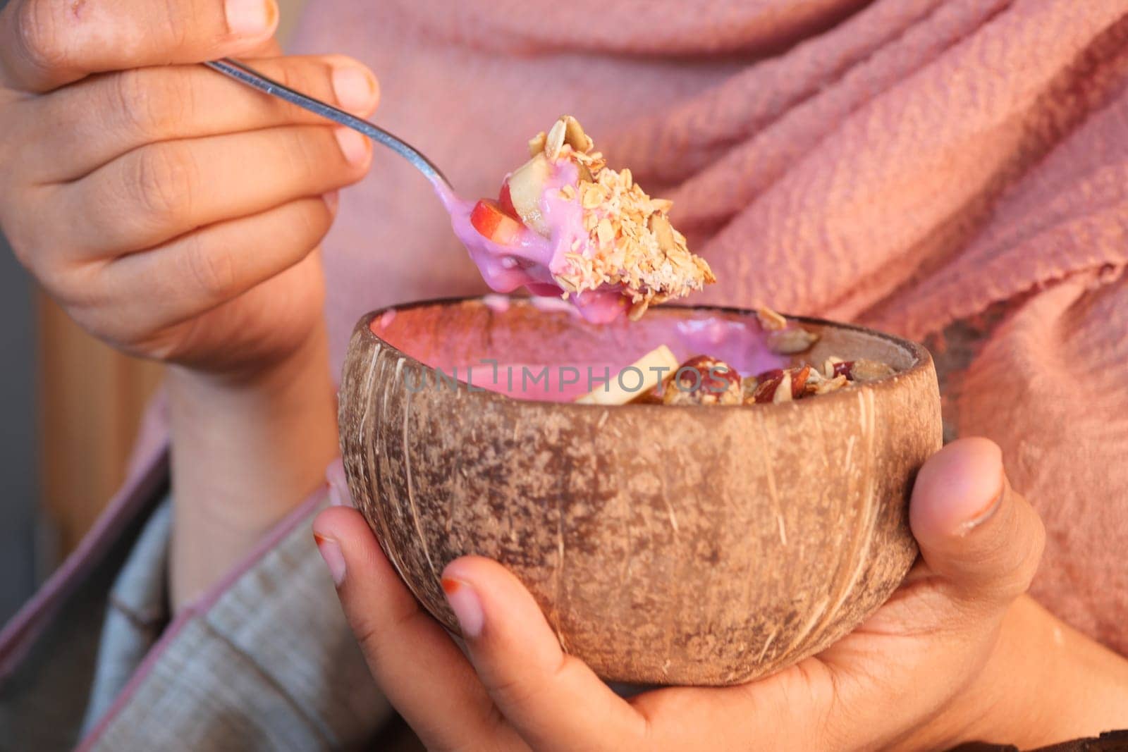 Hands hold a coconut bowl filled with vibrant dessert, enjoying the treat.
