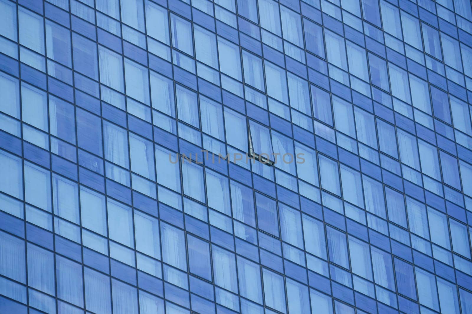 A modern glass building features a clear blue facade with one window missing.