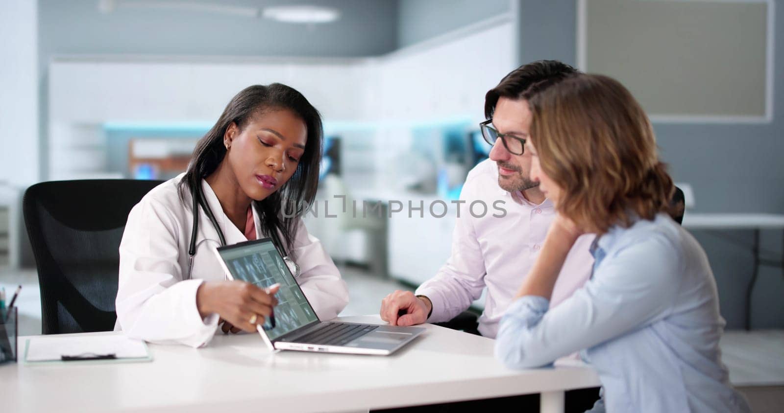 Doctor holding x-ray shows broken knee bone to patient on computer.