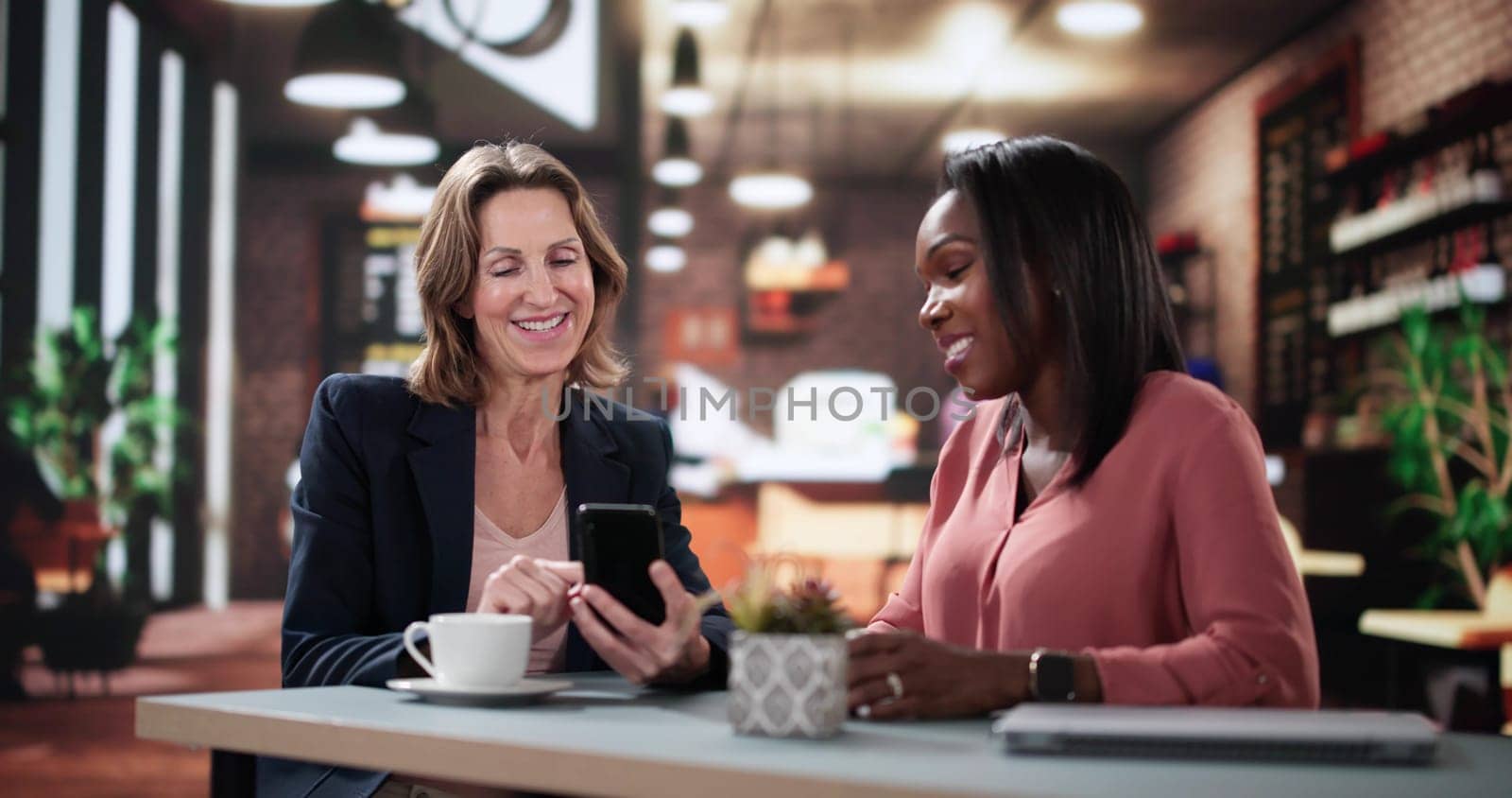 Woman smiling shows friend digital app on smartphone screen happily. Smart programmer and financial analyst sharing online project results over coffee