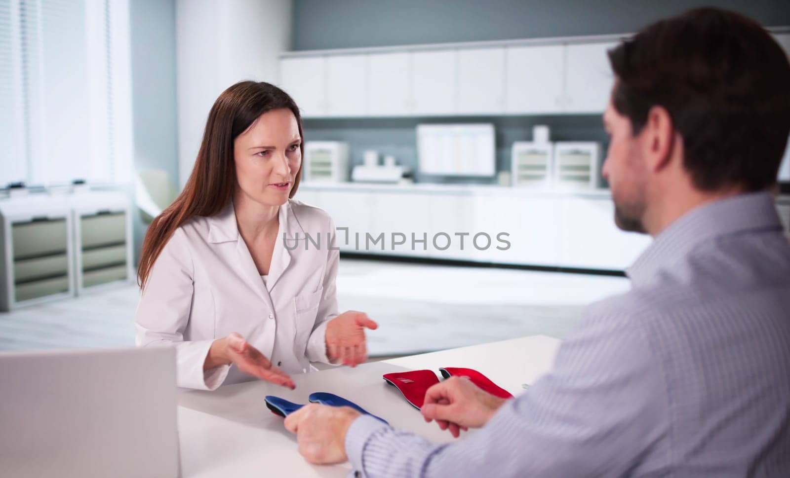 Expert orthopedist consults patient on orthopedic shoe insole for therapy.