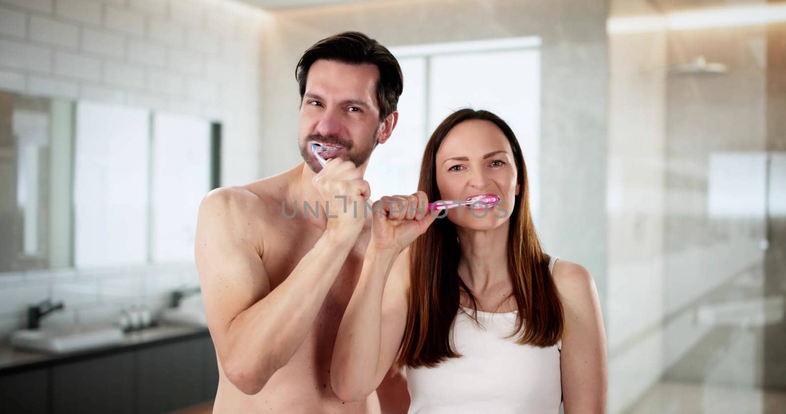 Smiling couple happily brushing teeth with electric toothbrush in bathroom. Beautiful woman and handsome man taking care of dental hygiene. , enjoying a moment