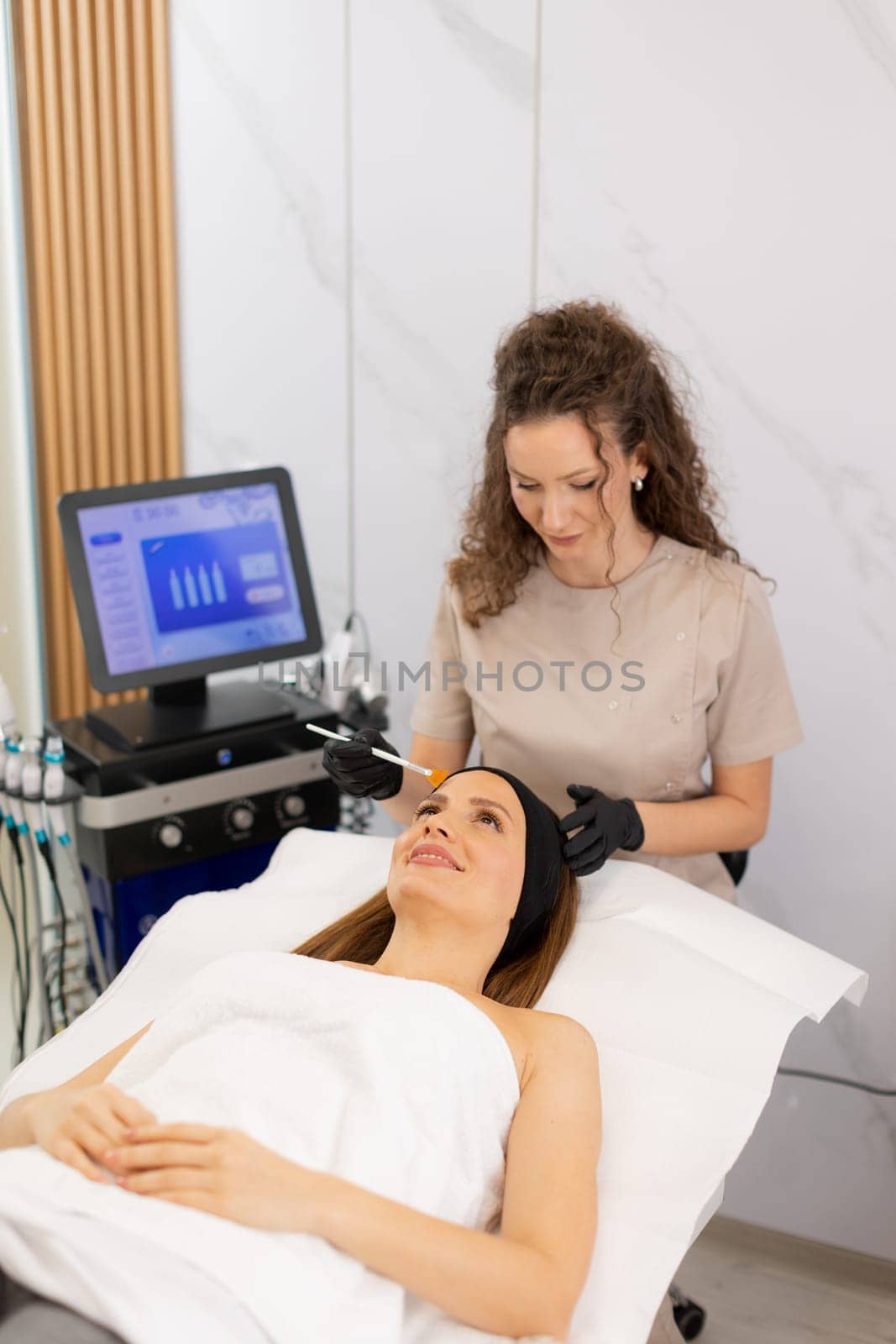 A woman enjoys a luxurious skincare treatment, lying on a treatment bed while a skilled aesthetician gently applies a soothing serum to her face in a serene spa environment.