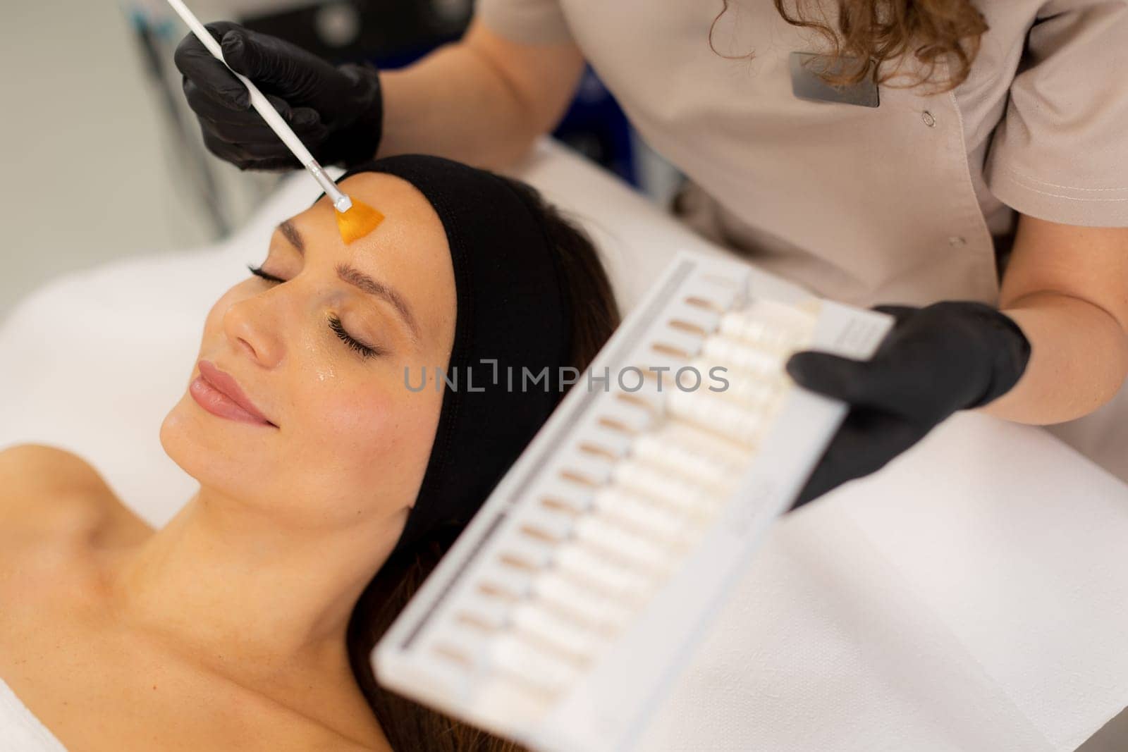 A skilled aesthetician gently applies a vibrant retinol serum to a client's forehead, enhancing her skincare routine in a tranquil spa setting filled with soothing decor.