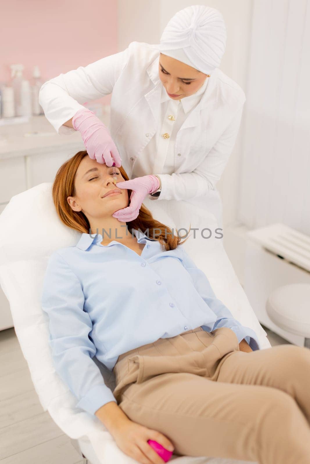 A woman enjoys a refreshing skincare procedure, lying comfortably as a skilled practitioner applies nourishing serum. The atmosphere is calming, promoting relaxation and wellness.