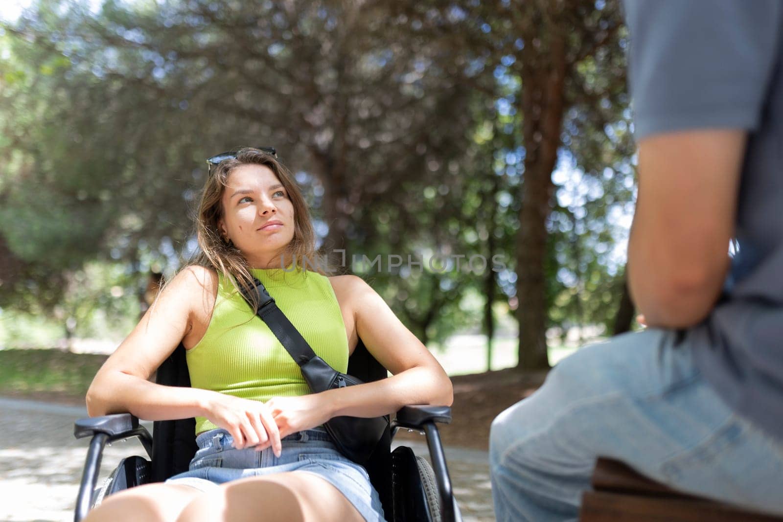 Young woman sitting in wheelchair talking with friend in park during summer