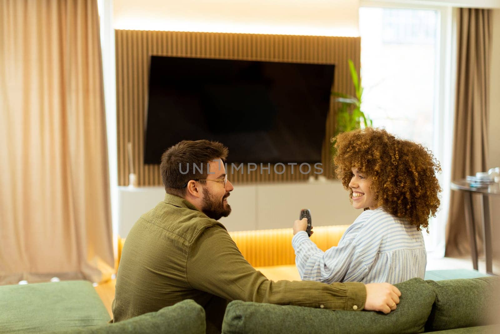Seated on a comfortable couch, a couple shares a light-hearted moment, laughing and watching their favorite show while surrounded by a warm, inviting atmosphere.
