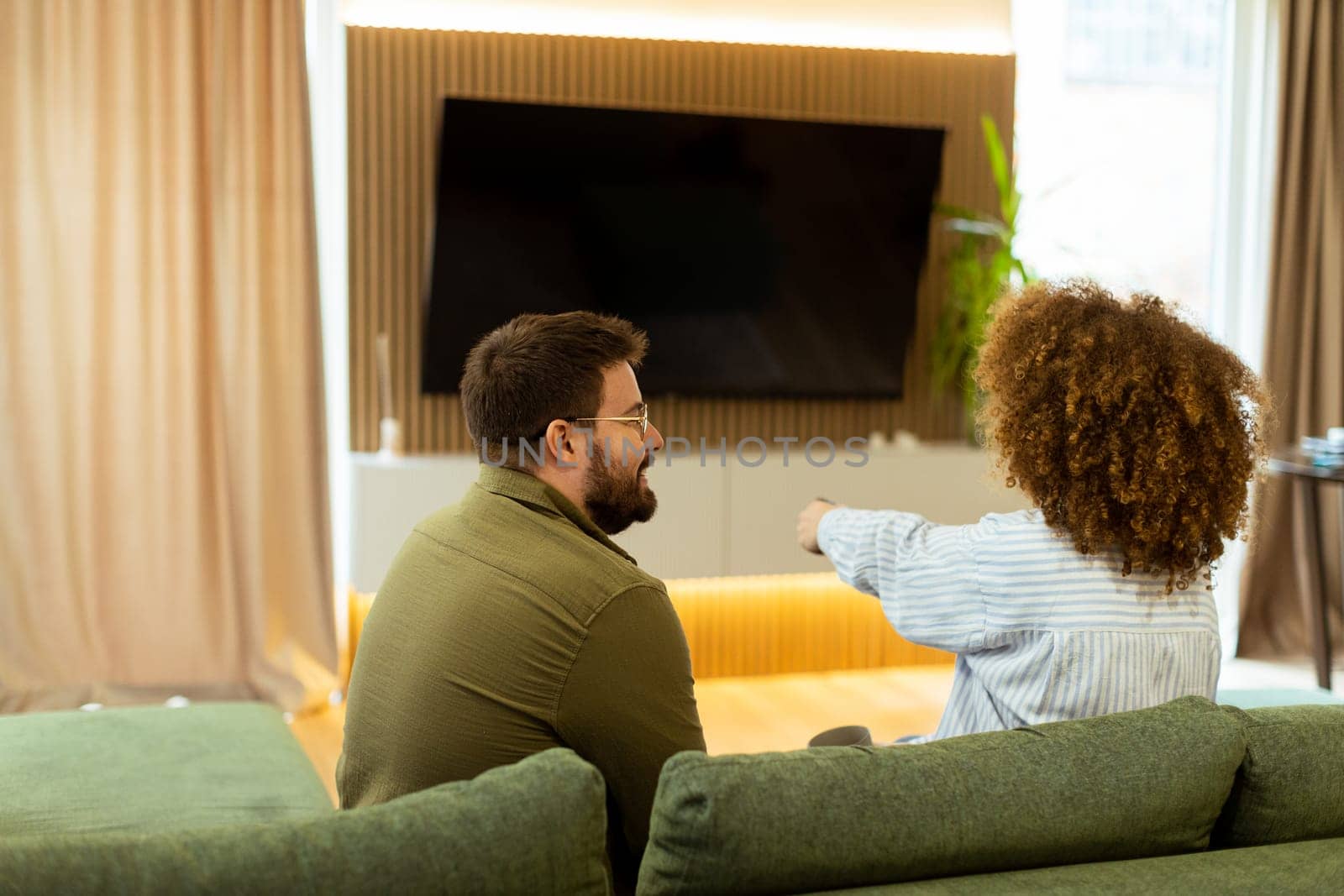 Seated on a comfortable couch, a couple shares a light-hearted moment, laughing and watching their favorite show while surrounded by a warm, inviting atmosphere.