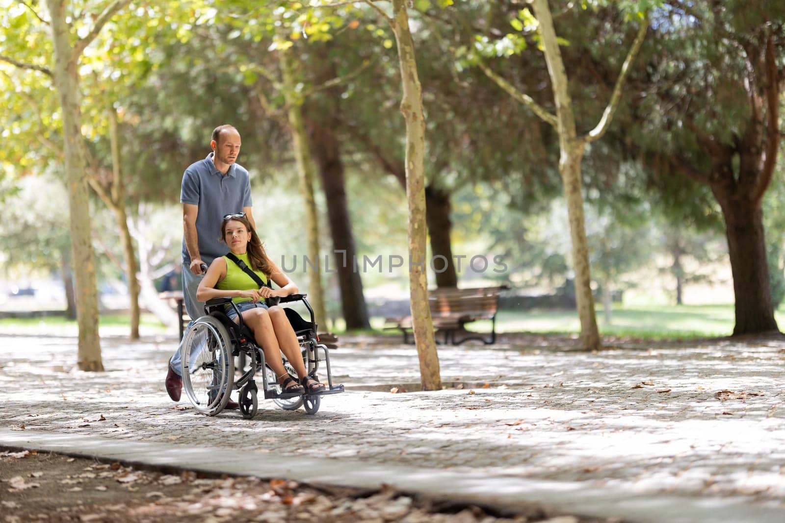 Man assisting a disabled woman in a wheelchair, enjoying a walk through a sunny park