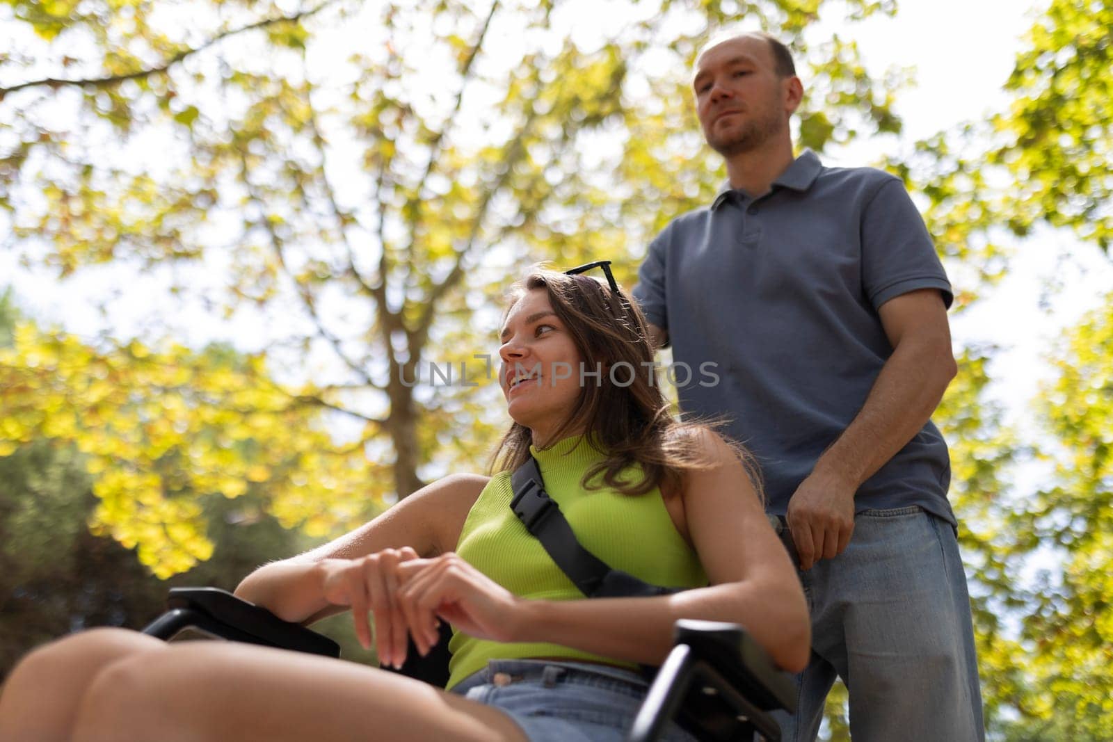 Nurse pushing a smiling disabled woman in a wheelchair through a sunny park during a summer day