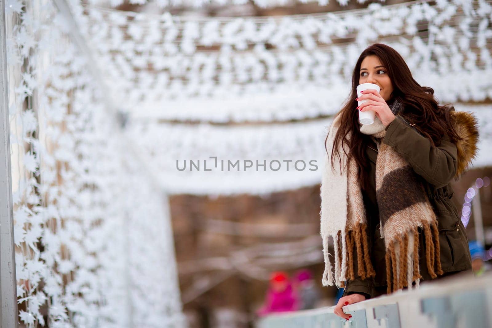Portrait of young woman in a snow park drinks tea at Christmas market