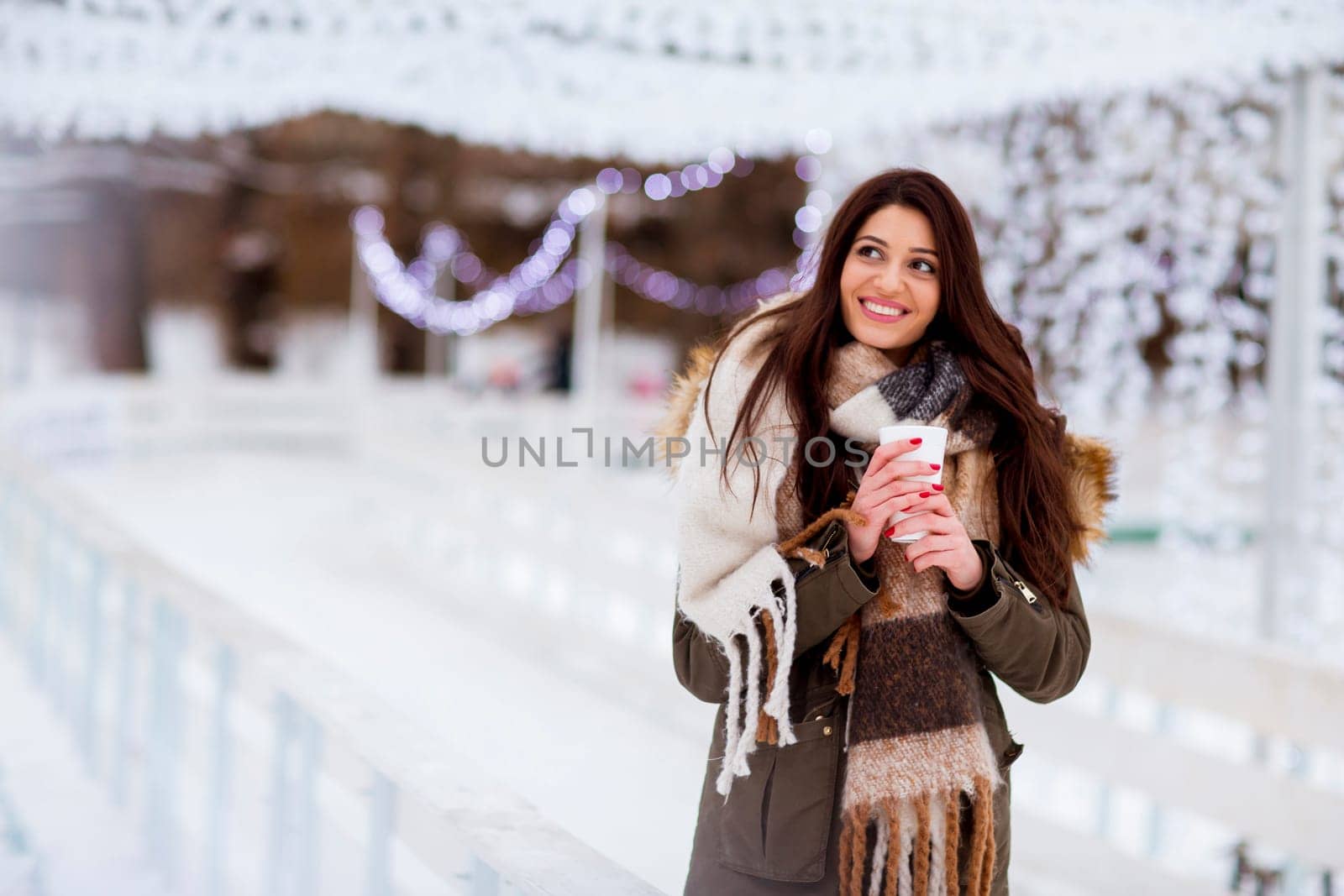 Portrait of young woman in a snow park drinks tea at Christmas market