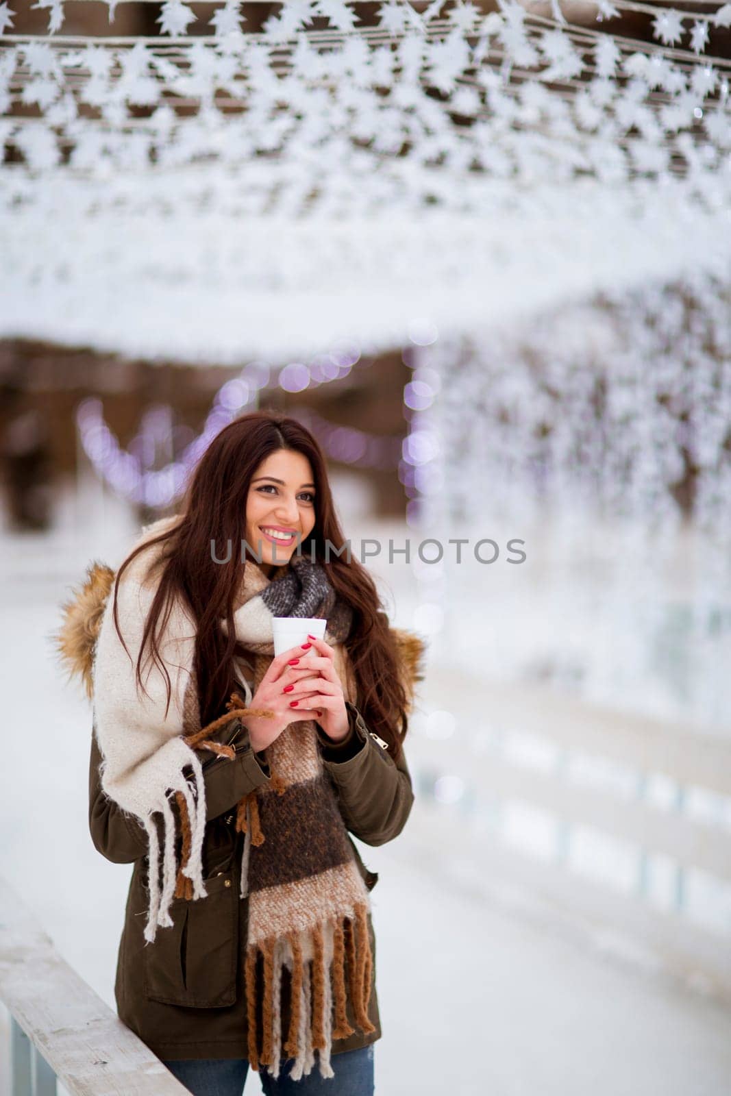 Portrait of young woman in a snow park drinks tea at Christmas market