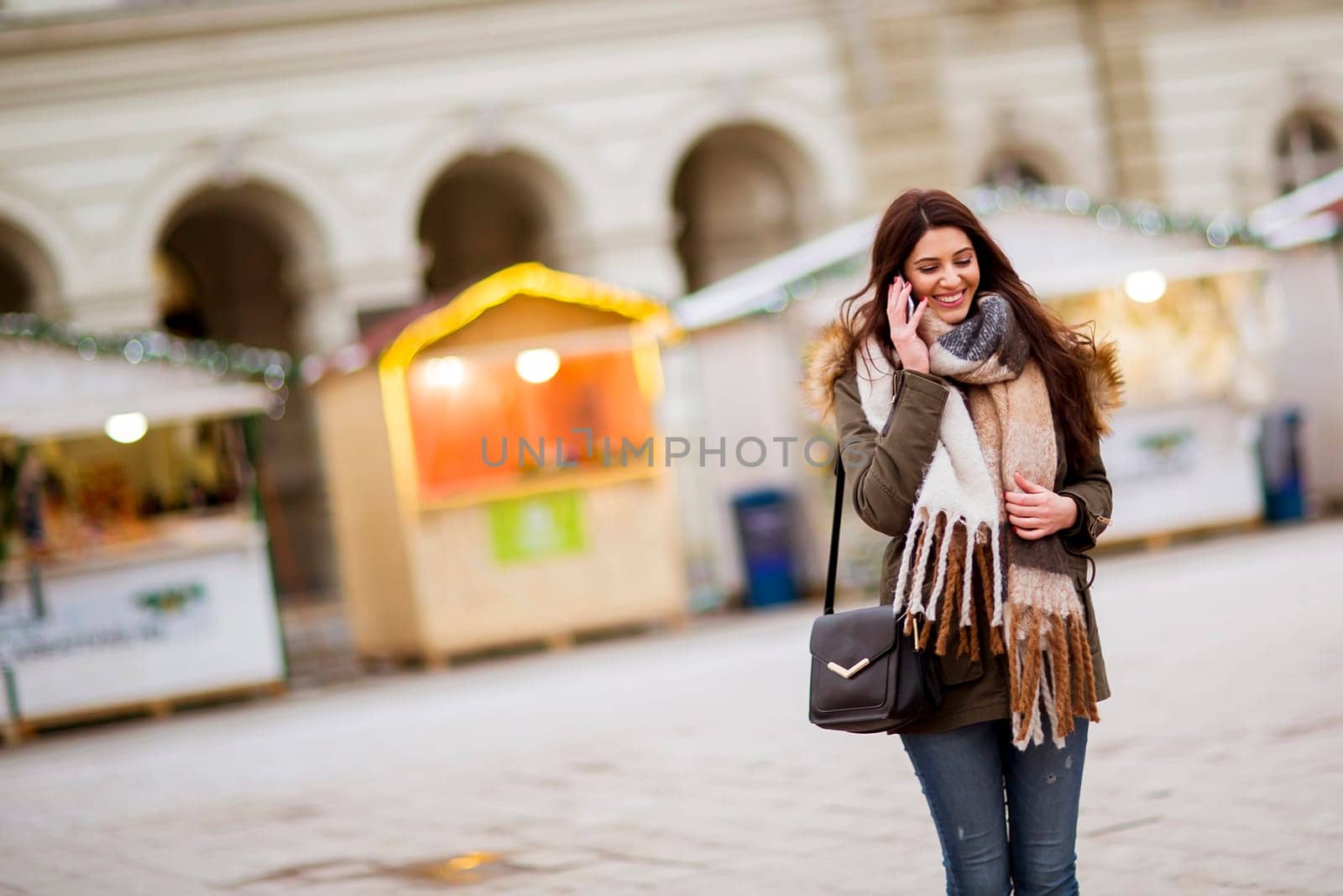 Portrait of smiling young woman using phoneon street at cold winter day